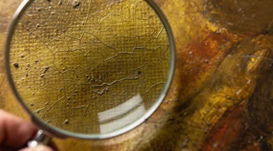 Expert examining an unsigned painting with a magnifying glass to identify visual dating clues